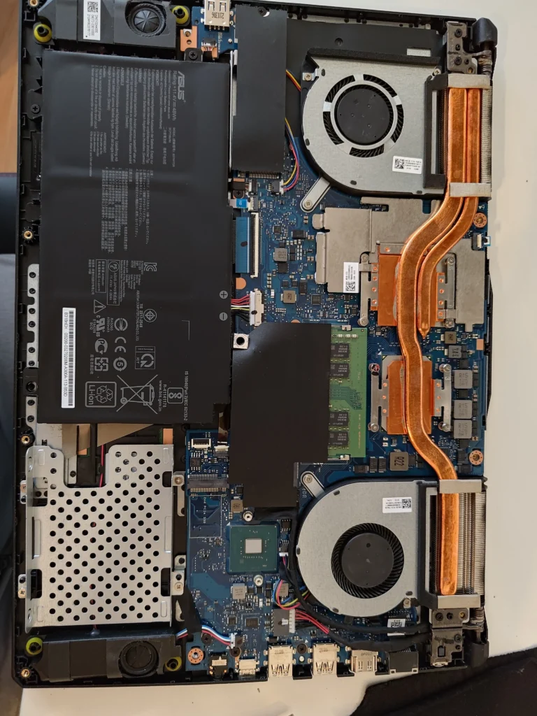 Opened ASUS FX506LH gaming laptop showing battery, two fans and copper pipes