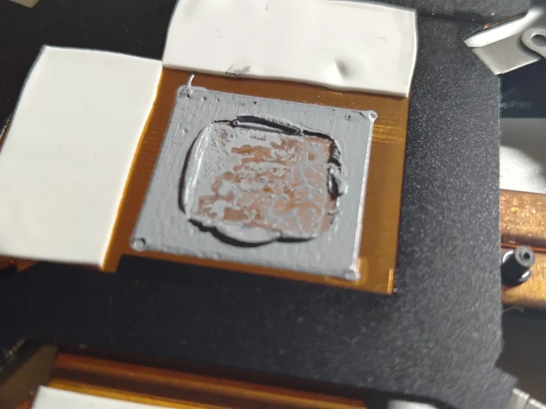 Old grey thermal paste remaining on a copper heatsink contact plate beside white thermal pads