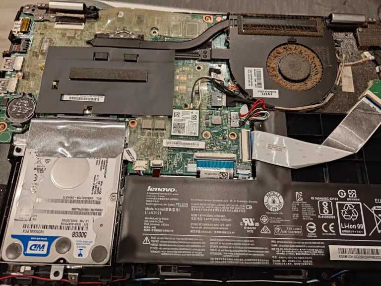 Opened Lenovo laptop showing hard drive bay, battery and dusty cooling fan