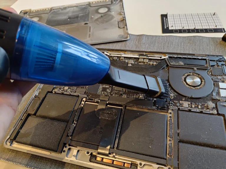 Air and brush tool cleaning an opened MacBook Pro 16-inch fan area