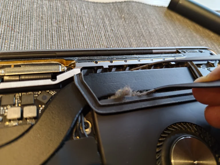 Lint clump lifted from the MacBook Pro A2141 rear outlet beside a fan